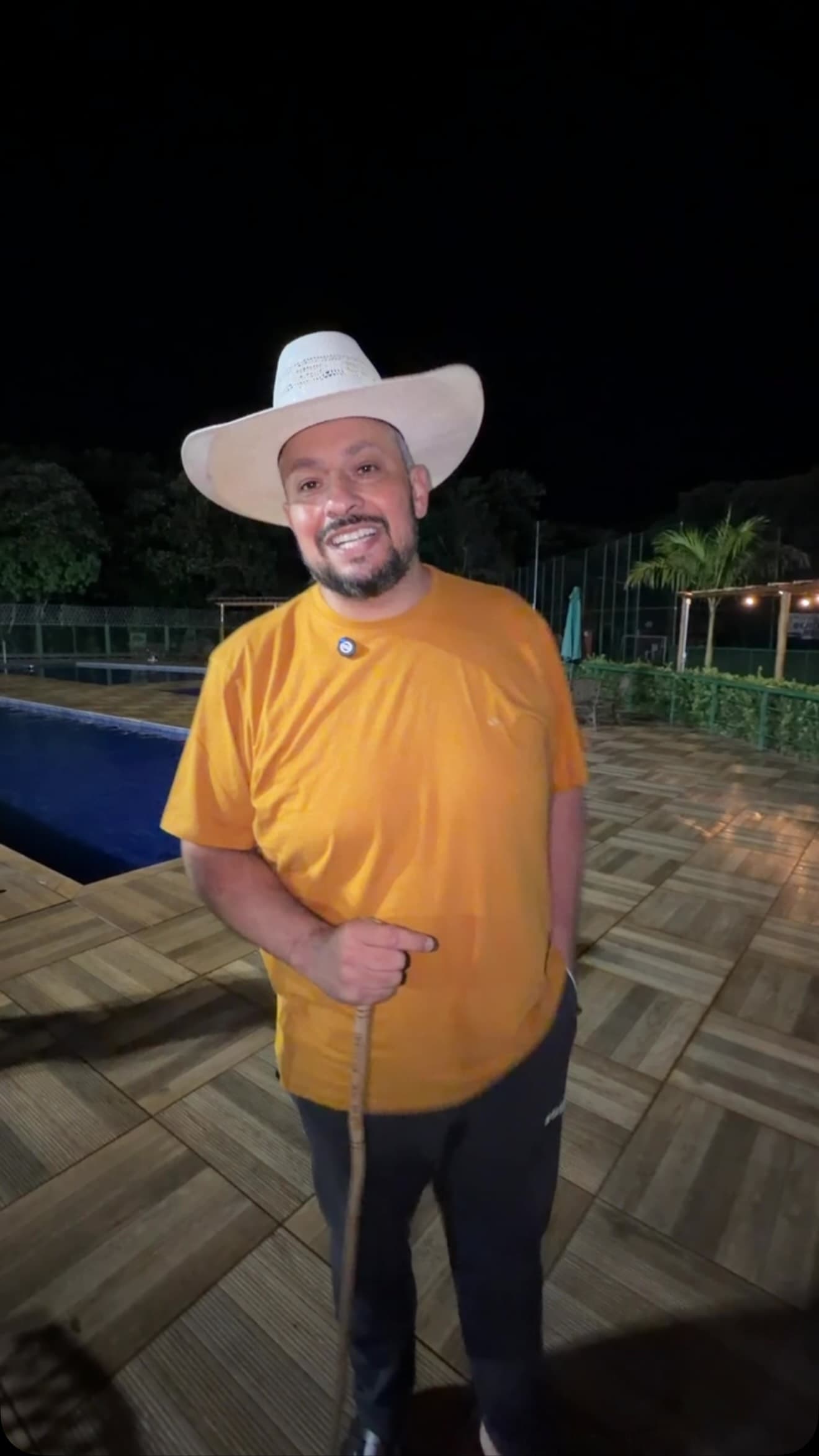 O pastor da Uai à noite, de chapéu branco e camiseta amarela, com o cajado na mão